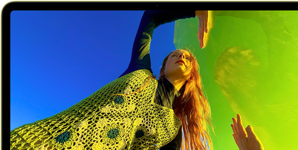 MacBook Neo, citrus color, screen shows a smiling person lying in a sunny field of flowers