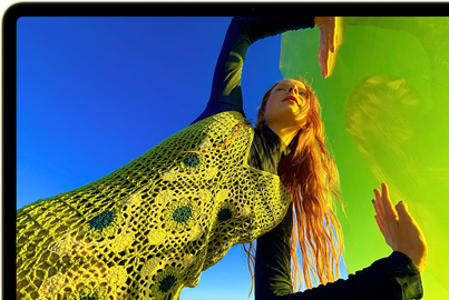 MacBook Neo, citrus color, screen shows a smiling person lying in a sunny field of flowers